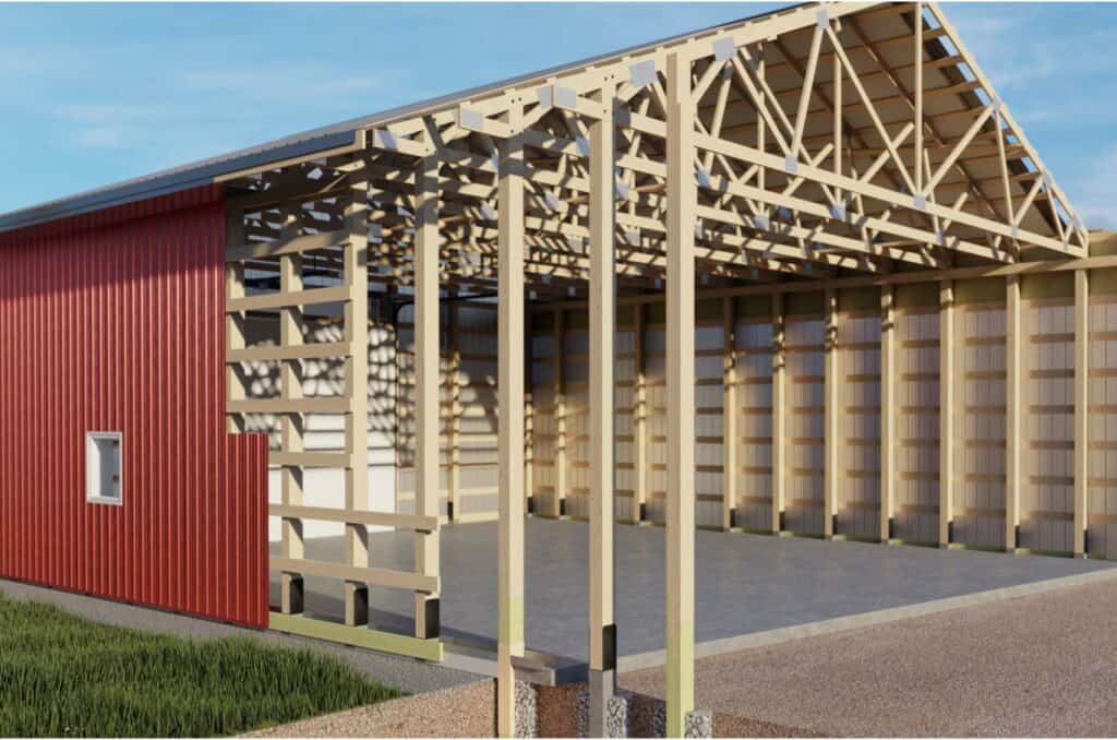 Partially constructed building with an exposed wooden frame, open roof trusses, and red metal siding on one side, standing on a concrete foundation under a blue sky.
