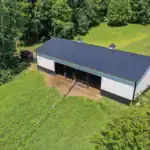 Drone view of post-frame barn with asphalt driveway and manicured lawn in rural Holmes County.