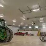 Spacious equipment storage facility in Walhonding, OH, built by Swiss Construction, with high ceilings, overhead lighting, mezzanine loft, and a parked John Deere tractor.