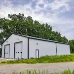 Custom white metal workshop with black trim and two oversized garage doors, built by Swiss Construction in Sunbury, Ohio, surrounded by open field and mature trees.