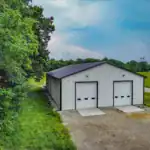 Front view of custom post-frame workshop with symmetrical garage doors and black metal roof, designed by Swiss Construction in Sunbury, Ohio, surrounded by rural landscape.