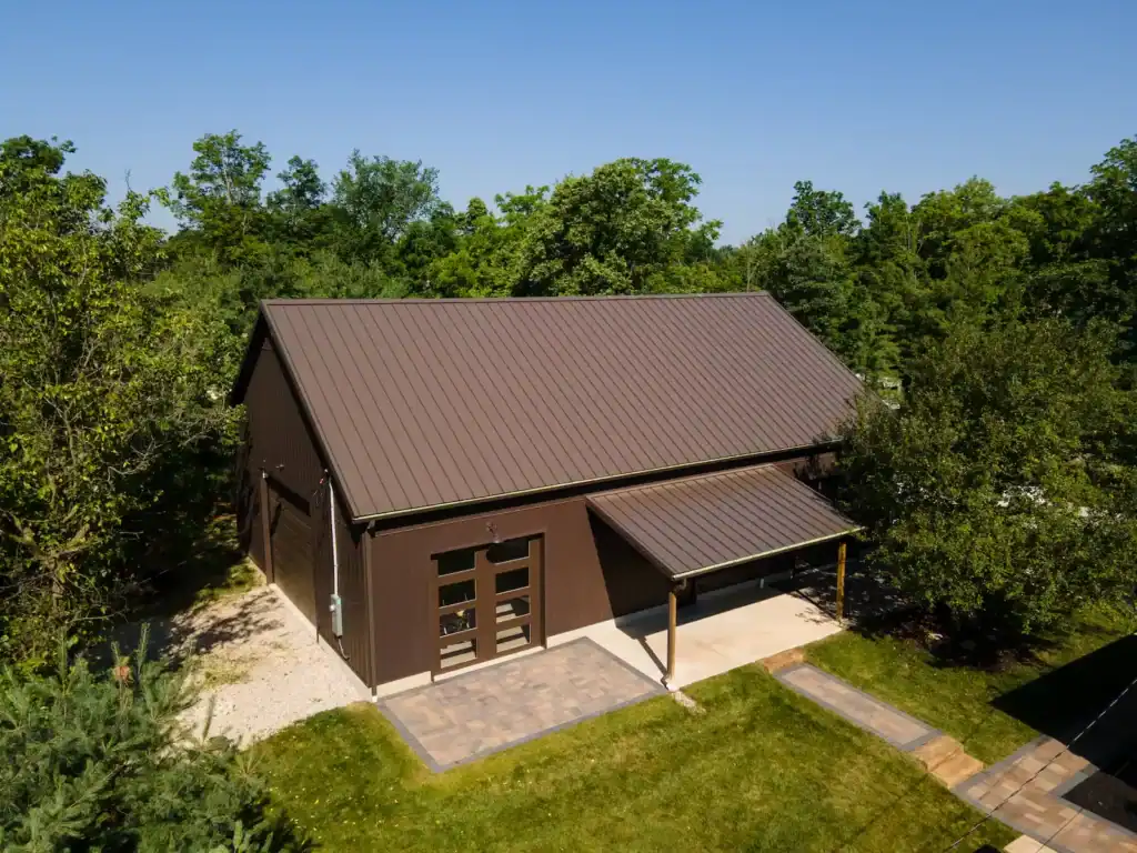 Aerial photo of of a modern brown barn-style building with metal roof, surrounded by trees