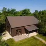 Aerial photo of of a modern brown barn-style building with metal roof, surrounded by trees