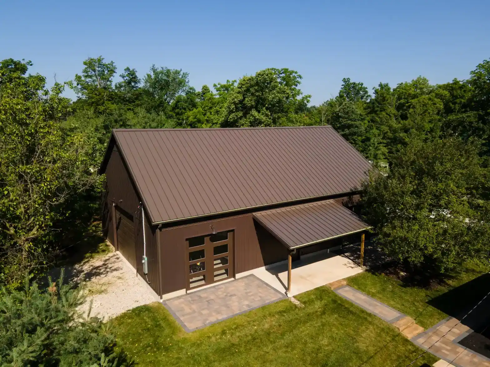 Aerial photo of of a modern brown barn-style building with metal roof, surrounded by trees