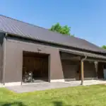 Brown barn-style building, Swiss Construction, with metal roof, open garage, and porch
