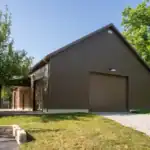 Brown barn-style building by Swiss Construction, with garage door and gravel drive