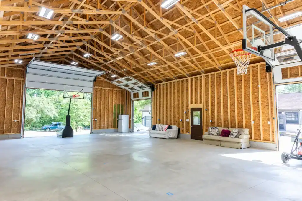 Large barn interior with exposed wood framing, concrete floor, basketball hoop