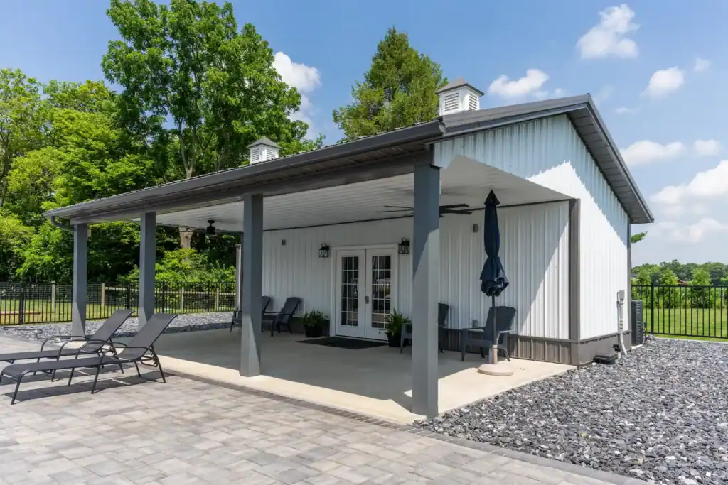 Modern Swiss Construction pool house with covered patio, lounge chairs, and paved outdoor space on a sunny day