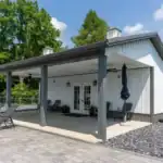 Modern Swiss Construction pool house with covered patio, lounge chairs, and paved outdoor space on a sunny day