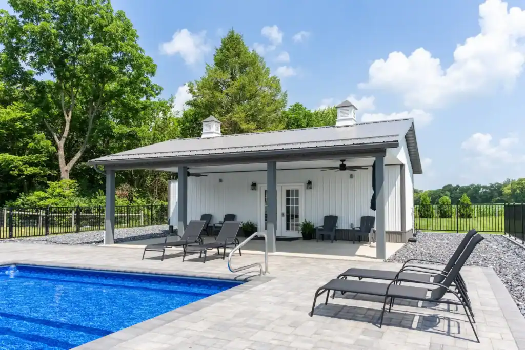 Sunny outdoor scene with white Swiss Construction pool house, blue swimming pool, and lounge chairs