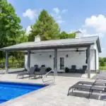 Sunny outdoor scene with white Swiss Construction pool house, blue swimming pool, and lounge chairs