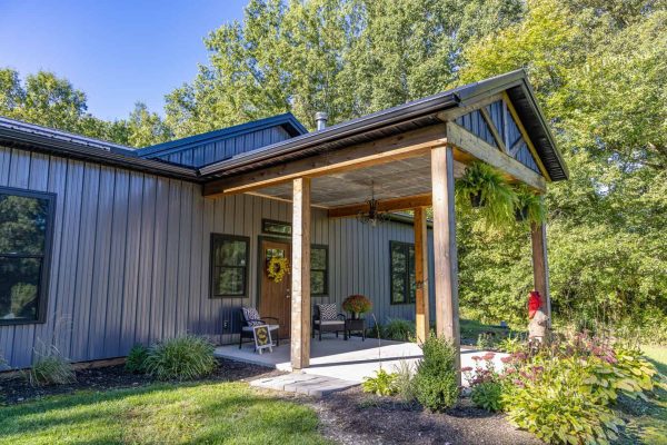 Covered front porch with timber columns, metal roof, and landscaped entryway, emphasizing the custom exterior details of this Brinkhaven-based barndominium by Swiss Construction.