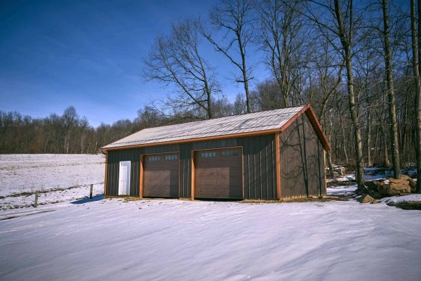 Rear corner view of insulated pole barn garage with carriage-style garage doors and snow-covered landscape.